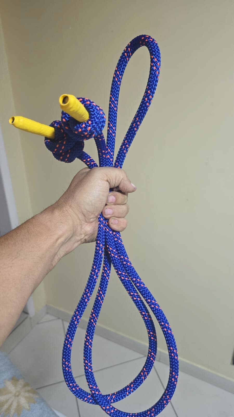 A corda azul de 11 mm segurada na mão: o nó da empunhadura, as duas ponteiras amarelas e os fios coral espalhados pela trança.