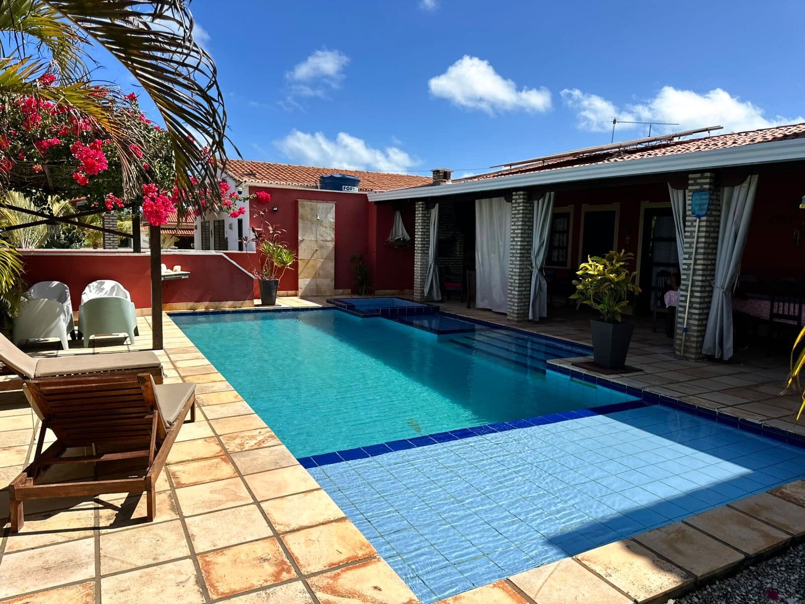 A piscina da casa com a prainha de borda e as espreguiçadeiras ao sol